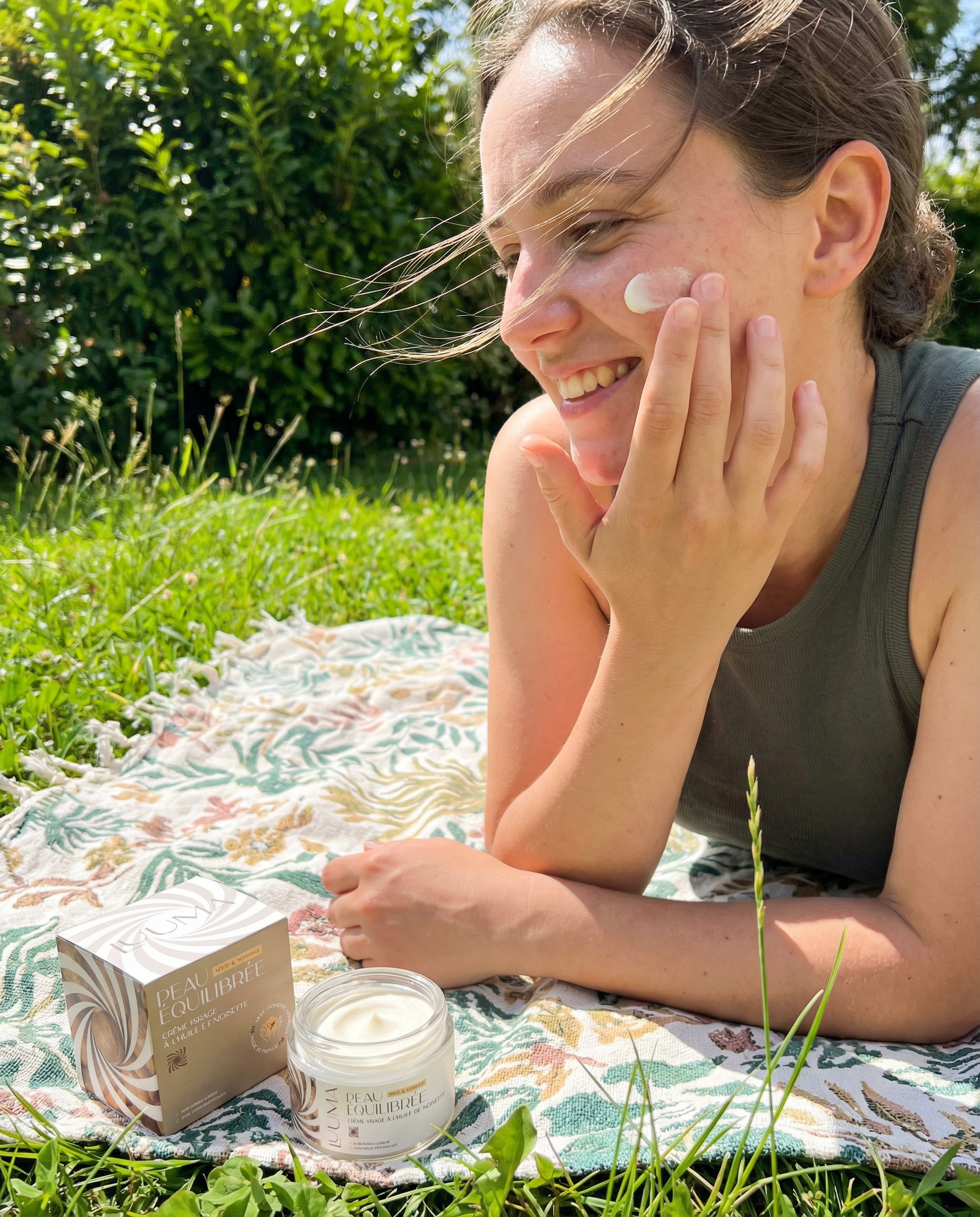 Une jeune femme allongée sur l'herbe utilise la creme